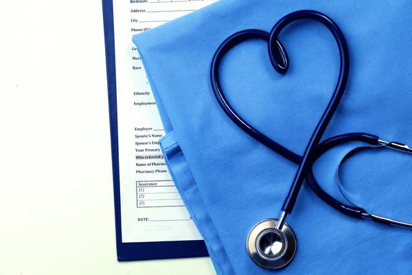 Estetoscopio médico retorcido en forma de corazón que se encuentra en la lista de antecedentes médicos del paciente y primer plano uniforme médico azul —  Fotos de Stock