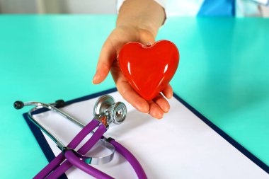 Kadın doktor kalp tutan stetoskop ile. Doktor ve hasta arka planda oturan