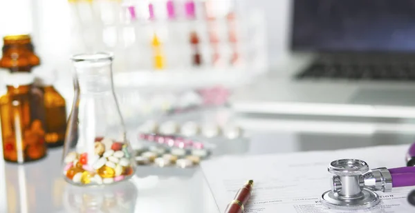 Primer plano del escritorio de un consultorio médico con un estetoscopio en primer plano y una botella con pastillas en el fondo — Foto de Stock