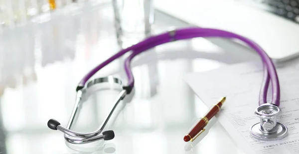Closeup of the desk of a doctors office with a stethoscope in the foreground and a bottle with pills in the background — Stock Photo, Image