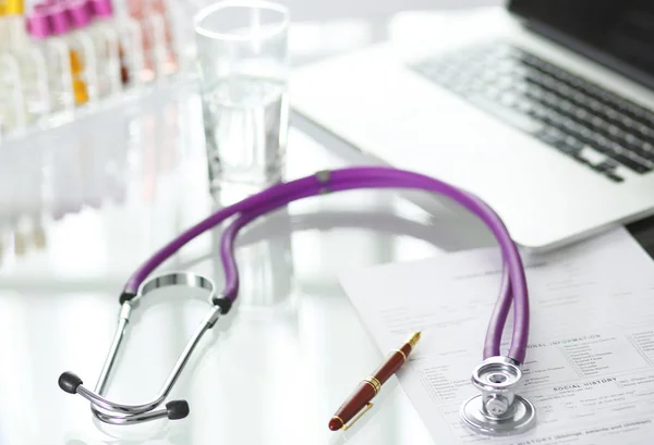 Primer plano del escritorio de un consultorio médico con un estetoscopio en primer plano y una botella con pastillas en el fondo — Foto de Stock