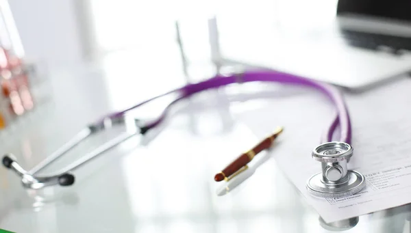 Closeup of the desk of a doctors office with a stethoscope in the foreground and a bottle with pills in the background — Stock Photo, Image