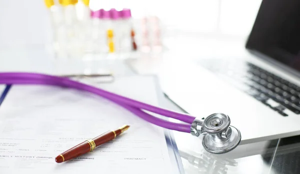 Closeup of the desk of a doctors office with a stethoscope in the foreground and a bottle with pills in the background — Stock Photo, Image