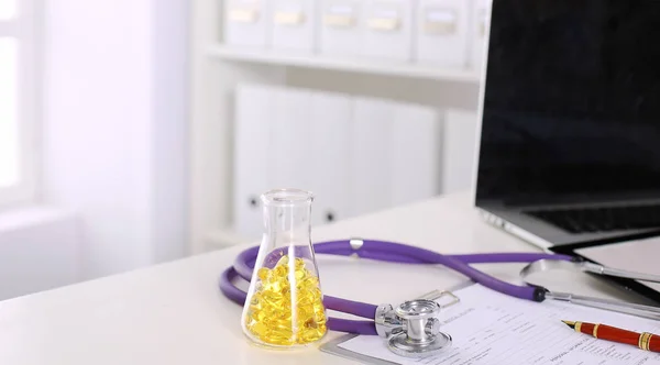 Primer plano del escritorio de un consultorio médico con un estetoscopio en primer plano y una botella con pastillas en el fondo — Foto de Stock