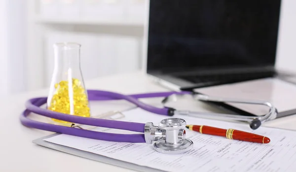 Zbliżenie na biurko w biurze lekarzy stetoskopem na pierwszym planie i butelkę z pigułki w tle — Zdjęcie stockowe