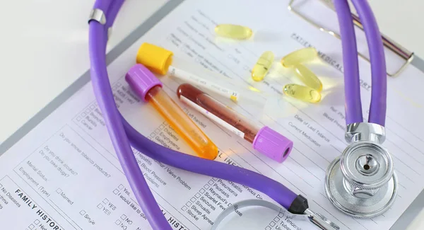 Primer plano del escritorio de un consultorio médico con un estetoscopio en primer plano y una botella con pastillas en el fondo — Foto de Stock