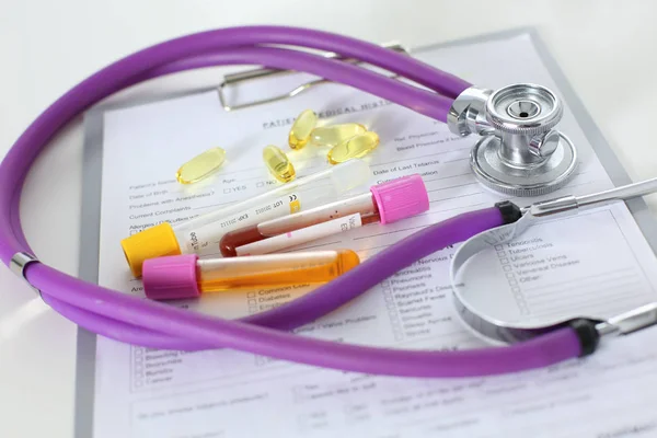 Closeup of the desk of a doctors office with a stethoscope in the foreground and a bottle with pills in the background — Stock Photo, Image