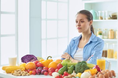 mutlu genç ev hanımı bir kazık çeşitli taze organik meyve ve sebze gıda hazırlama mutfakta oturmuş