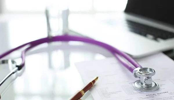 Primer plano del escritorio de un consultorio médico con un estetoscopio en primer plano y una botella con pastillas en el fondo — Foto de Stock