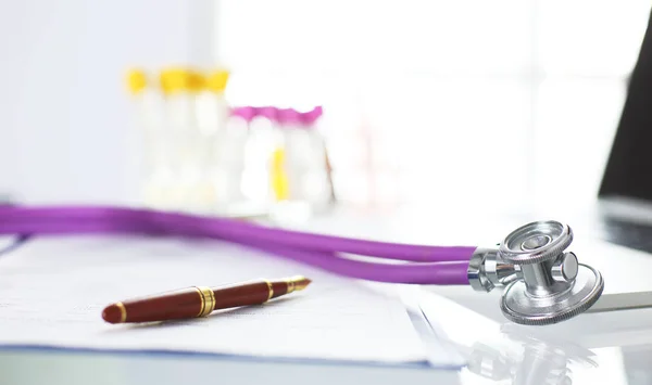 Close-up da mesa de um consultório médico com um estetoscópio em primeiro plano e uma garrafa com pílulas no fundo — Fotografia de Stock