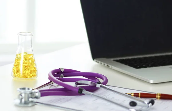 Close-up da mesa de um consultório médico com um estetoscópio em primeiro plano e uma garrafa com pílulas no fundo — Fotografia de Stock