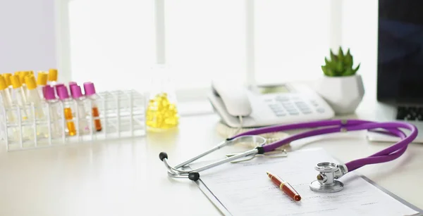 Primer plano del escritorio de un consultorio médico con un estetoscopio en primer plano y una botella con pastillas en el fondo —  Fotos de Stock