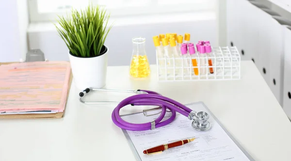 Primer plano del escritorio de un consultorio médico con un estetoscopio en primer plano y una botella con pastillas en el fondo — Foto de Stock