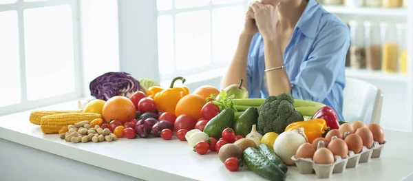 Gelukkig jonge huisvrouw zit in de keuken bereiden van voedsel uit een stapel van diverse verse biologische groenten en fruit — Stockfoto