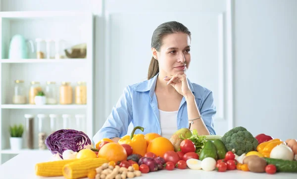 快乐的年轻主妇坐在厨房准备食物从一堆不同的新鲜有机水果和蔬菜 — 图库照片