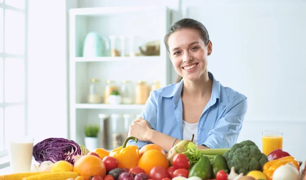 Glückliche junge Hausfrau, die in der Küche sitzt und aus einem Haufen frischem Bio-Obst und -Gemüse Essen zubereitet — Stockfoto