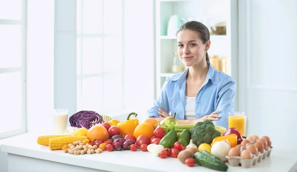 Glückliche junge Hausfrau, die in der Küche sitzt und aus einem Haufen frischem Bio-Obst und -Gemüse Essen zubereitet — Stockfoto
