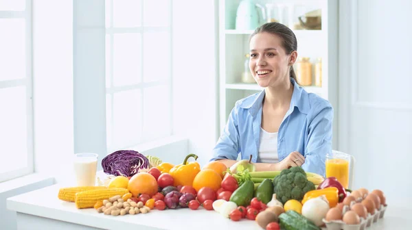 多様の新鮮な有機性果物と野菜の山からの食糧を準備する台所に座って幸せな若い主婦 — ストック写真