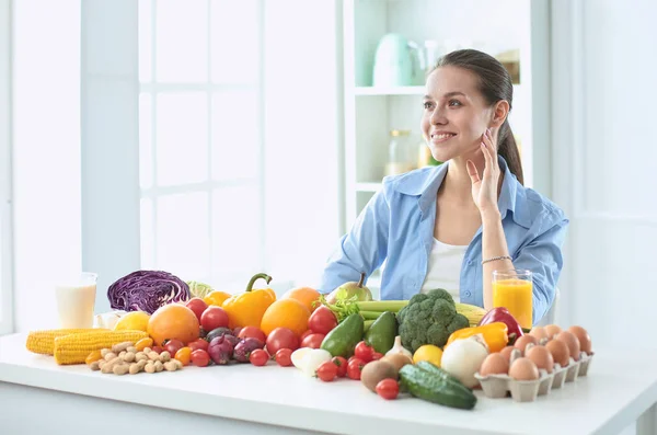 多様の新鮮な有機性果物と野菜の山からの食糧を準備する台所に座って幸せな若い主婦 — ストック写真