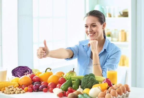 Glückliche junge Hausfrau, die in der Küche sitzt und aus einem Haufen frischem Bio-Obst und -Gemüse Essen zubereitet — Stockfoto