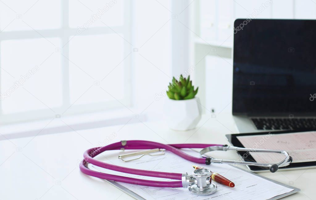 closeup of the desk of a doctors office with a stethoscope in the foreground and a bottle with pills in the background