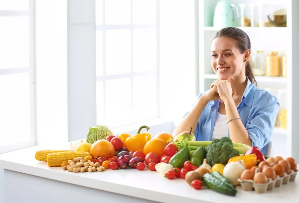 Glückliche junge Hausfrau, die in der Küche sitzt und aus einem Haufen frischem Bio-Obst und -Gemüse Essen zubereitet — Stockfoto