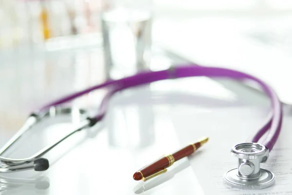 Closeup of the desk of a doctors office with a stethoscope in the foreground and a bottle with pills in the background — Stock Photo, Image