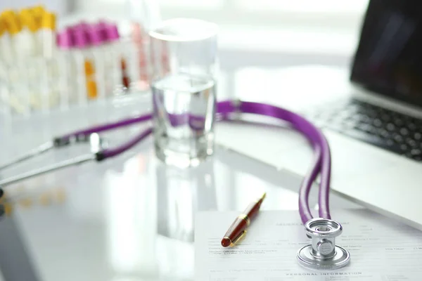 Closeup of the desk of a doctors office with a stethoscope in the foreground and a bottle with pills in the background — Stock Photo, Image