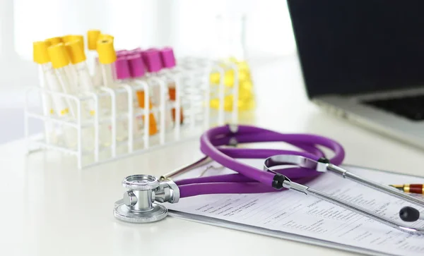 Primer plano del escritorio de un consultorio médico con un estetoscopio en primer plano y una botella con pastillas en el fondo — Foto de Stock