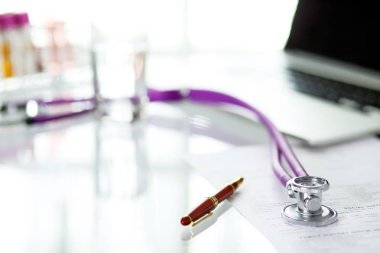 closeup of the desk of a doctors office with a stethoscope in the foreground and a bottle with pills in the background clipart