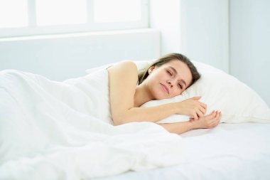 Genç güzellik beyaz bir yatakta uyuyor