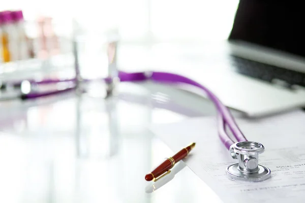 Nahaufnahme vom Schreibtisch einer Arztpraxis mit einem Stethoskop im Vordergrund und einer Flasche mit Pillen im Hintergrund — Stockfoto