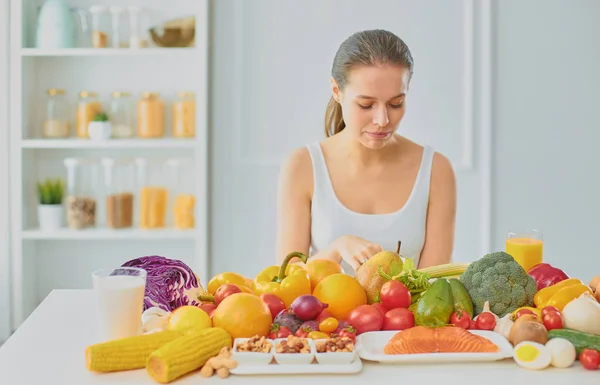 Mutlu genç ev hanımı bir kazık çeşitli taze organik meyve ve sebze gıda hazırlama mutfakta oturmuş — Stok fotoğraf