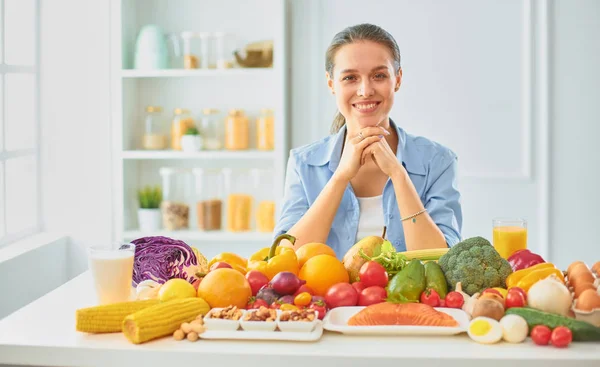 Glad Ung hemmafru sitter i köket förbereder mat från en hög med olika färska ekologiska frukter och grönsaker — Stockfoto