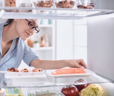 Mutlu kadın açık buzdolabı önünde sebzeli