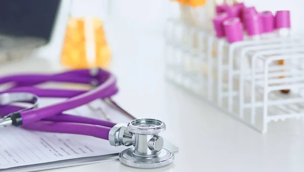 Closeup of the desk of a doctors office with a stethoscope in the foreground and a bottle with pills in the background — Stock Photo, Image