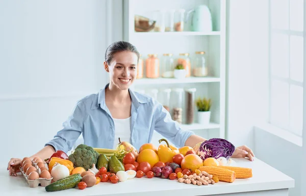 Щаслива молода домогосподарка сидить на кухні готує їжу з купи різноманітних свіжих органічних фруктів і овочів — стокове фото