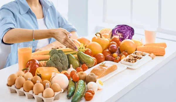 多様の新鮮な有機性果物と野菜の山からの食糧を準備する台所に座って幸せな若い主婦 — ストック写真