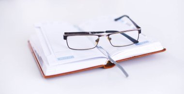 Masanın üstünde an açık defter üzerinde gözlük yalan