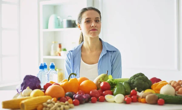 Mutlu genç ev hanımı bir kazık çeşitli taze organik meyve ve sebze gıda hazırlama mutfakta oturmuş — Stok fotoğraf