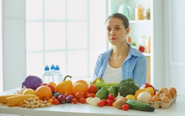 çeşitli taze organik meyve ve sebze, seçici odak bir kazık yiyecek hazırlama mutfakta oturup mutlu genç ev hanımı