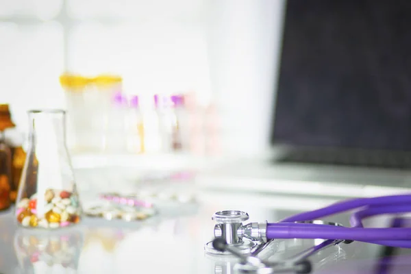 Nahaufnahme vom Schreibtisch einer Arztpraxis mit einem Stethoskop im Vordergrund und einer Flasche mit Pillen im Hintergrund, selektiver Fokus — Stockfoto