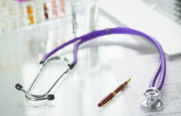 Closeup of the desk of a doctors office with a stethoscope in the foreground and a bottle with pills in the background, selective focus — Stock Photo, Image