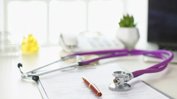 Closeup of the desk of a doctors office with a stethoscope in the foreground and a bottle with pills in the background, selective focus — Stock Photo, Image