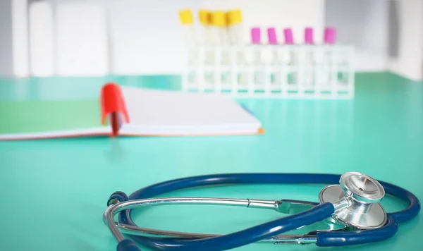 Close-up da mesa de um consultório médico com um estetoscópio em primeiro plano e uma garrafa com pílulas no fundo, foco seletivo — Fotografia de Stock