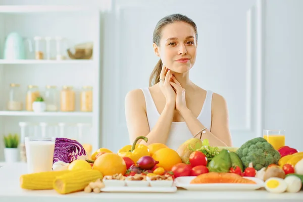 Glückliche junge Hausfrau, die in der Küche sitzt und aus einem Stapel verschiedenster frischer Bio-Früchte und -Gemüse Nahrung zubereitet, selektiver Fokus — Stockfoto