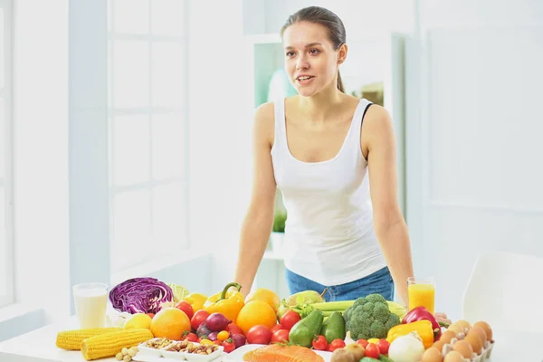 Jovem dona de casa feliz sentado na cozinha preparando alimentos de uma pilha de frutas e legumes orgânicos frescos diversos, foco seletivo — Fotografia de Stock