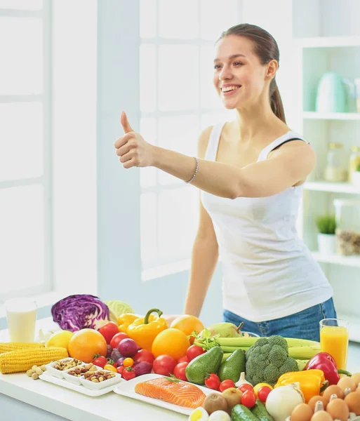 Glückliche junge Hausfrau, die in der Küche sitzt und aus einem Stapel verschiedenster frischer Bio-Früchte und -Gemüse Nahrung zubereitet, selektiver Fokus — Stockfoto