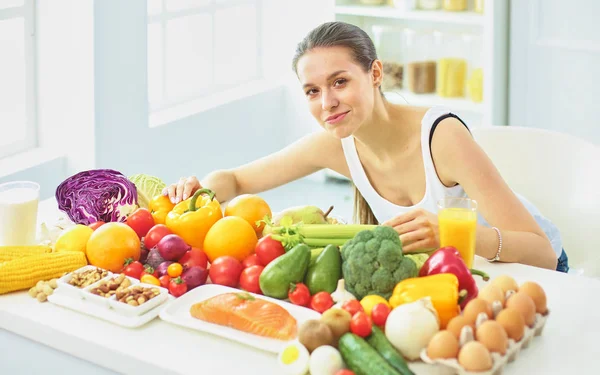 Glad Ung hemmafru sitter i köket förbereder mat från en hög av olika färska ekologiska frukter och grönsaker, selektivt fokus — Stockfoto