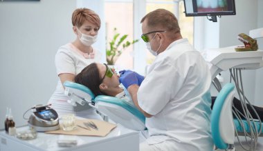 Doktor dişçi genç ve güzel bir kızın dişlerini tedavi ediyor. Dişçinin resepsiyonundaki kız. Doktor dişçi dişleri tedavi eder.